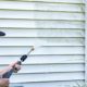 woman power washing the outside of her home - LoonShine Exterior Services safe siding cleaning methods